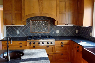 Kitchen - mid-sized craftsman u-shaped ceramic tile kitchen idea in New York with a farmhouse sink, recessed-panel cabinets, medium tone wood cabinets, soapstone countertops, gray backsplash, stone tile backsplash, stainless steel appliances and an island