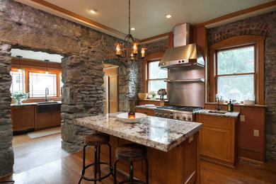 Example of a large arts and crafts l-shaped medium tone wood floor open concept kitchen design in Kansas City with a farmhouse sink, flat-panel cabinets, medium tone wood cabinets, granite countertops, stainless steel appliances and an island