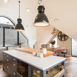 This is an example of a medium sized scandinavian l-shaped kitchen/diner in Oxfordshire with a belfast sink, shaker cabinets, grey cabinets, integrated appliances, medium hardwood flooring, an island and brown floors.