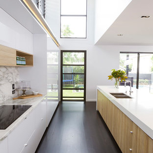 This is an example of a large contemporary galley kitchen in Brisbane with dark hardwood floors, with island, flat-panel cabinets, white cabinets, grey splashback, brown floor and white benchtop.