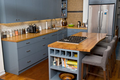 Example of a mid-sized transitional l-shaped light wood floor eat-in kitchen design in New York with wood countertops, an island, stainless steel appliances, a drop-in sink, flat-panel cabinets, blue cabinets, white backsplash and ceramic backsplash