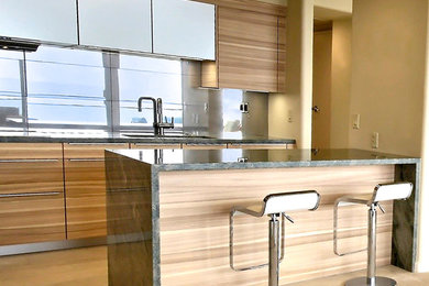 Moderne Wohnküche in L-Form mit Unterbauwaschbecken, flächenbündigen Schrankfronten, hellbraunen Holzschränken, Granit-Arbeitsplatte, Küchenrückwand in Metallic, Rückwand aus Spiegelfliesen und Küchengeräten aus Edelstahl in Hawaii