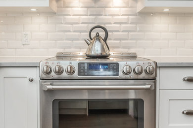 Inspiration for a mid-sized transitional u-shaped light wood floor and gray floor eat-in kitchen remodel in Toronto with white cabinets, white backsplash, stainless steel appliances, no island, a double-bowl sink, raised-panel cabinets, marble countertops and subway tile backsplash