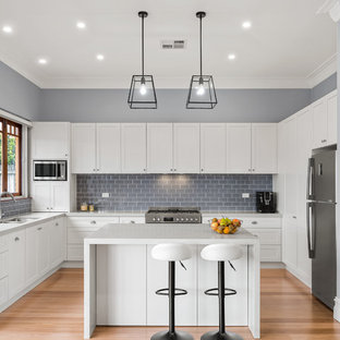 This is an example of a mid-sized transitional u-shaped open plan kitchen in Sydney with an undermount sink, shaker cabinets, white cabinets, quartz benchtops, grey splashback, ceramic splashback, stainless steel appliances, light hardwood floors, with island, brown floor and grey benchtop.