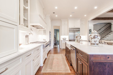 Inspiration for a transitional l-shaped medium tone wood floor kitchen remodel in Atlanta with a farmhouse sink, white cabinets, stainless steel appliances and an island