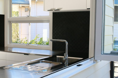 Foto de cocina contemporánea con fregadero integrado, salpicadero negro, suelo de madera oscura y una isla