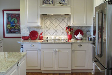 Example of a classic medium tone wood floor kitchen design in Chicago with an undermount sink, raised-panel cabinets, white cabinets, granite countertops, white backsplash, ceramic backsplash and stainless steel appliances