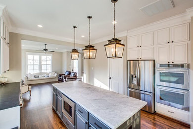 Inspiration for a large victorian l-shaped medium tone wood floor and brown floor open concept kitchen remodel in Houston with a farmhouse sink, recessed-panel cabinets, white cabinets, marble countertops, gray backsplash, stone tile backsplash, stainless steel appliances and an island