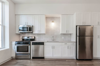 This is an example of a modern kitchen in Chicago with shaker cabinets, white cabinets, engineered stone countertops, white splashback, ceramic splashback, stainless steel appliances, light hardwood flooring, no island, grey floors, white worktops and a submerged sink.