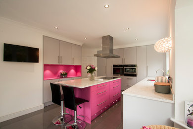 This is an example of a large contemporary grey and pink u-shaped kitchen in Surrey with flat-panel cabinets, grey cabinets, composite countertops, ceramic flooring, an island, grey floors, a submerged sink, pink splashback, black appliances and white worktops.