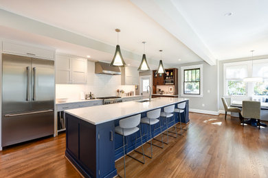 Design ideas for a large traditional galley open plan kitchen in DC Metro with a submerged sink, shaker cabinets, blue cabinets, engineered stone countertops, white splashback, metro tiled splashback, stainless steel appliances, medium hardwood flooring, an island, brown floors and grey worktops.