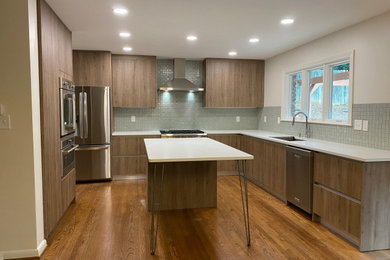 Example of a mid-sized 1960s u-shaped medium tone wood floor kitchen design in Atlanta with an undermount sink, flat-panel cabinets, brown cabinets, quartz countertops, green backsplash, mosaic tile backsplash, stainless steel appliances, an island and white countertops
