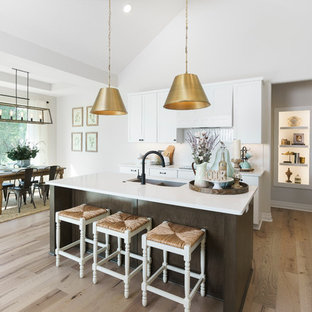 This is an example of a mid-sized scandinavian l-shaped open plan kitchen in Wichita with a double-bowl sink, quartzite benchtops, white splashback, ceramic splashback, stainless steel appliances, light hardwood floors, with island, brown floor, white benchtop, flat-panel cabinets and brown cabinets.