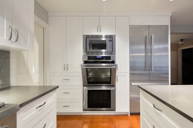 Inspiration for a mid-sized contemporary single-wall medium tone wood floor eat-in kitchen remodel with flat-panel cabinets, white cabinets, gray backsplash, glass tile backsplash, stainless steel appliances, a peninsula and an undermount sink