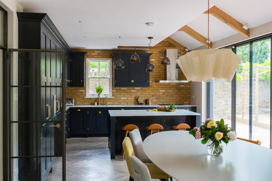 This is an example of a medium sized contemporary kitchen/diner in London with a submerged sink, black cabinets, light hardwood flooring, an island and grey floors.
