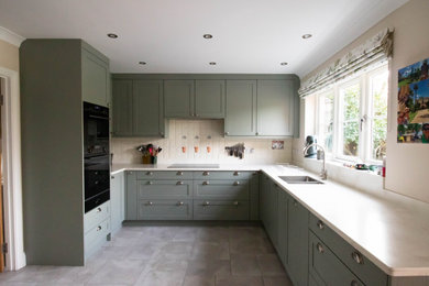 Inspiration for a classic u-shaped kitchen/diner in Oxfordshire with a built-in sink, shaker cabinets, green cabinets, composite countertops, white splashback, ceramic splashback, black appliances, ceramic flooring, no island, grey floors and white worktops.