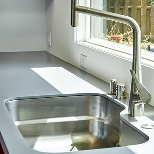 Offene, Mittelgroße Moderne Küche in U-Form mit Unterbauwaschbecken, flächenbündigen Schrankfronten, roten Schränken, Mineralwerkstoff-Arbeitsplatte, Küchengeräten aus Edelstahl, Kücheninsel und grauer Arbeitsplatte in San Francisco