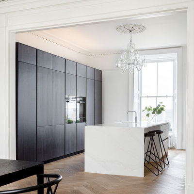 Kitchen - contemporary galley medium tone wood floor and brown floor kitchen idea in Dublin with an undermount sink, flat-panel cabinets, dark wood cabinets, an island and white countertops