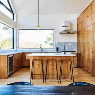Cette photo montre une grand cuisine américaine tendance en L avec un évier encastré, des portes de placard en bois brun, un plan de travail en marbre, une crédence blanche, une crédence en marbre, un électroménager encastrable, un sol en bois clair, un îlot central, un plan de travail blanc et un plafond voûté.