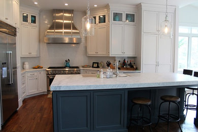 Inredning av ett klassiskt kök, med en undermonterad diskho, blå skåp, marmorbänkskiva, vitt stänkskydd, stänkskydd i tunnelbanekakel, rostfria vitvaror, mellanmörkt trägolv och en köksö