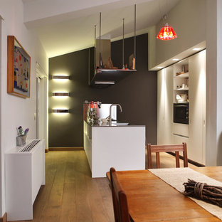 Immagine di una cucina design di medie dimensioni con ante bianche, top in laminato, elettrodomestici bianchi, pavimento in legno massello medio, penisola, lavello integrato, ante lisce e paraspruzzi a effetto metallico