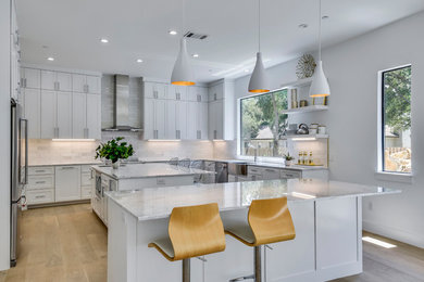 Inspiration for a large contemporary u-shaped light wood floor and beige floor open concept kitchen remodel in Austin with shaker cabinets, white cabinets, white backsplash, two islands, a farmhouse sink, quartzite countertops, stone tile backsplash, stainless steel appliances and white countertops