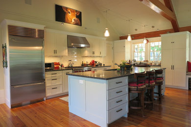 Inspiration for a mid-sized country galley dark wood floor and brown floor eat-in kitchen remodel in Boston with an undermount sink, shaker cabinets, white cabinets, granite countertops, green backsplash, glass tile backsplash, stainless steel appliances and an island