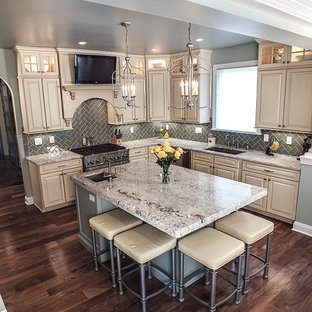 Photo of a large contemporary l-shaped eat-in kitchen in Cleveland with a drop-in sink, raised-panel cabinets, beige cabinets, granite benchtops, grey splashback, ceramic splashback, stainless steel appliances, dark hardwood floors and with island.