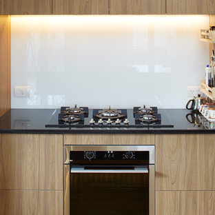 Ispirazione per un'ampia cucina minimal con lavello da incasso, ante di vetro, ante bianche, top in granito, paraspruzzi bianco, paraspruzzi con lastra di vetro, elettrodomestici neri, pavimento in compensato e penisola