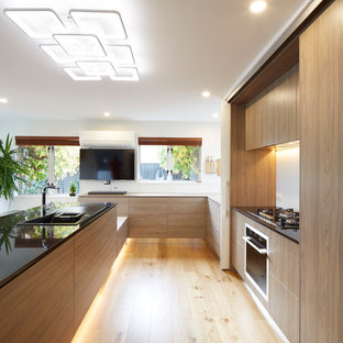 Inspiration pour une très grand cuisine américaine design en U avec un évier posé, un placard à porte vitrée, des portes de placard blanches, un plan de travail en granite, une crédence blanche, une crédence en feuille de verre, un électroménager noir, un sol en contreplaqué et une péninsule.