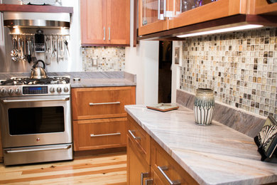 Example of a small trendy l-shaped light wood floor and brown floor enclosed kitchen design in Other with beaded inset cabinets, medium tone wood cabinets, quartzite countertops, multicolored backsplash, glass tile backsplash, stainless steel appliances and no island