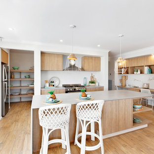 Beach style l-shaped kitchen in Melbourne with an undermount sink, flat-panel cabinets, medium wood cabinets, stainless steel appliances, medium hardwood floors, with island, brown floor and white benchtop.