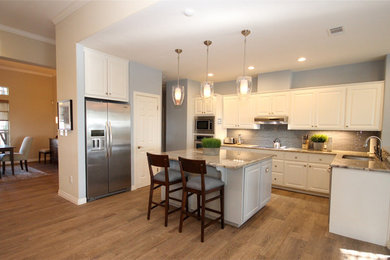 Inspiration for a large transitional l-shaped medium tone wood floor and brown floor enclosed kitchen remodel in Austin with raised-panel cabinets, white cabinets, granite countertops, gray backsplash, stainless steel appliances, an island, glass tile backsplash, an undermount sink and multicolored countertops