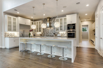 Example of a trendy light wood floor kitchen design in Austin with an undermount sink, shaker cabinets, white cabinets, quartz countertops, glass tile backsplash, stainless steel appliances, an island and white countertops