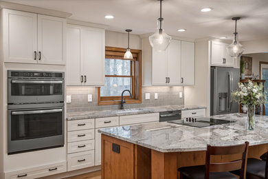 Example of a large l-shaped medium tone wood floor open concept kitchen design in Columbus with an undermount sink, shaker cabinets, white cabinets, granite countertops, gray backsplash, subway tile backsplash, an island and gray countertops