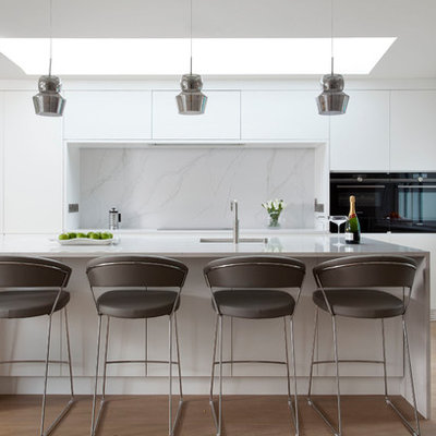 Example of a mid-sized trendy galley light wood floor and beige floor kitchen design in Dublin with flat-panel cabinets, white backsplash, marble backsplash, black appliances, an island, an undermount sink and marble countertops