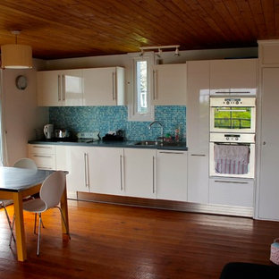 Design ideas for a small beach style single-wall eat-in kitchen in Sussex with a single-bowl sink, flat-panel cabinets, white cabinets, laminate benchtops, blue splashback, glass tile splashback, stainless steel appliances, medium hardwood floors and no island.