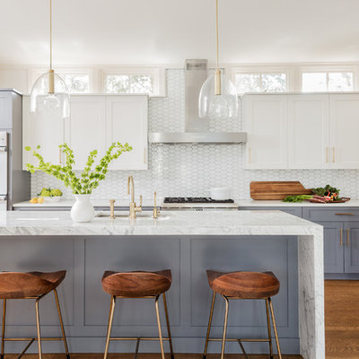 Mid-sized transitional l-shaped medium tone wood floor and brown floor kitchen photo in Boston with an undermount sink, marble countertops, white backsplash, glass tile backsplash, stainless steel appliances, an island, shaker cabinets and white cabinets