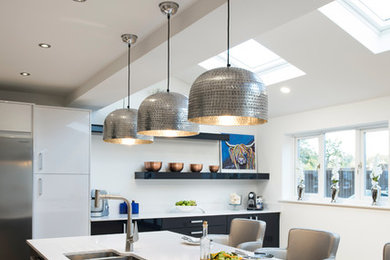 Design ideas for a large contemporary l-shaped open plan kitchen in West Midlands with a built-in sink, white cabinets, white splashback, stainless steel appliances, light hardwood flooring, a breakfast bar, beige floors and white worktops.