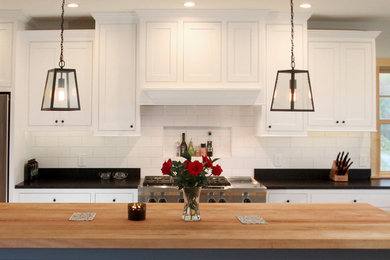 Bild på ett mellanstort lantligt kök, med luckor med profilerade fronter, vita skåp, träbänkskiva, vitt stänkskydd, stänkskydd i keramik, rostfria vitvaror, en köksö, ljust trägolv och en rustik diskho