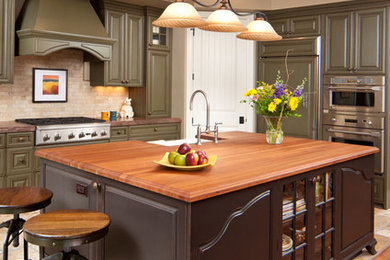 Immagine di un cucina con isola centrale chic con ante con bugna sagomata, ante verdi, paraspruzzi beige e elettrodomestici in acciaio inossidabile