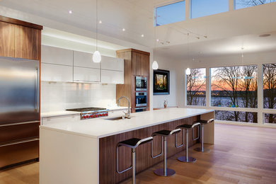 Example of a trendy galley light wood floor eat-in kitchen design in Portland with flat-panel cabinets, white cabinets, quartz countertops, white backsplash, glass sheet backsplash, stainless steel appliances, an island and a single-bowl sink