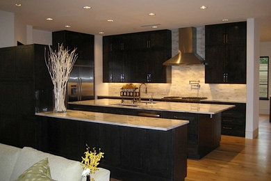 Photo of a medium sized contemporary u-shaped open plan kitchen in Dallas with a submerged sink, raised-panel cabinets, dark wood cabinets, beige splashback, stainless steel appliances, medium hardwood flooring, multiple islands and engineered stone countertops.
