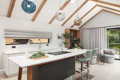 This is an example of a large contemporary galley kitchen in Other with a submerged sink, flat-panel cabinets, white cabinets, white splashback, integrated appliances, porcelain flooring, an island, beige floors and beige worktops.