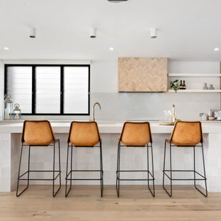 Inspiration for a beach style l-shaped kitchen in Sydney with flat-panel cabinets, medium wood cabinets, white splashback, panelled appliances, light hardwood floors, with island, beige floor and white benchtop.