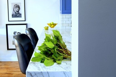 Mittelgroße Moderne Wohnküche in L-Form mit Landhausspüle, Schrankfronten mit vertiefter Füllung, blauen Schränken, Marmor-Arbeitsplatte, Küchenrückwand in Weiß, Rückwand aus Metrofliesen, Küchengeräten aus Edelstahl, braunem Holzboden und Kücheninsel in Los Angeles