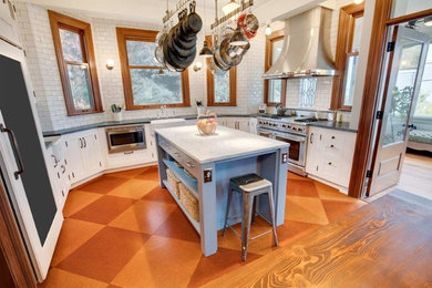 シアトルにある中くらいなカントリー風のおしゃれなキッチン (エプロンフロントシンク、シェーカースタイル扉のキャビネット、白いキャビネット、クオーツストーンカウンター、白いキッチンパネル、サブウェイタイルのキッチンパネル、白い調理設備、コルクフローリング、茶色い床) の写真
