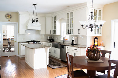 Inspiration for a large transitional l-shaped light wood floor eat-in kitchen remodel in Other with a farmhouse sink, white cabinets, granite countertops, white backsplash, subway tile backsplash, stainless steel appliances, an island and raised-panel cabinets