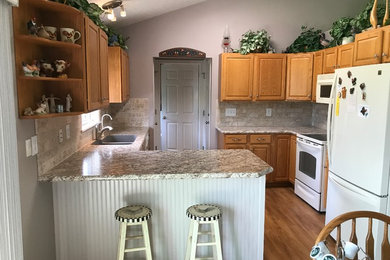 Medium sized classic l-shaped kitchen/diner in Grand Rapids with a submerged sink, raised-panel cabinets, medium wood cabinets, laminate countertops, stone tiled splashback, white appliances, laminate floors and a breakfast bar.
