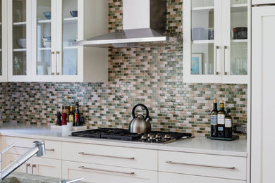 Example of a mid-sized trendy l-shaped eat-in kitchen design in Boston with glass-front cabinets, white cabinets, quartz countertops, an island, multicolored backsplash, ceramic backsplash, an undermount sink and stainless steel appliances